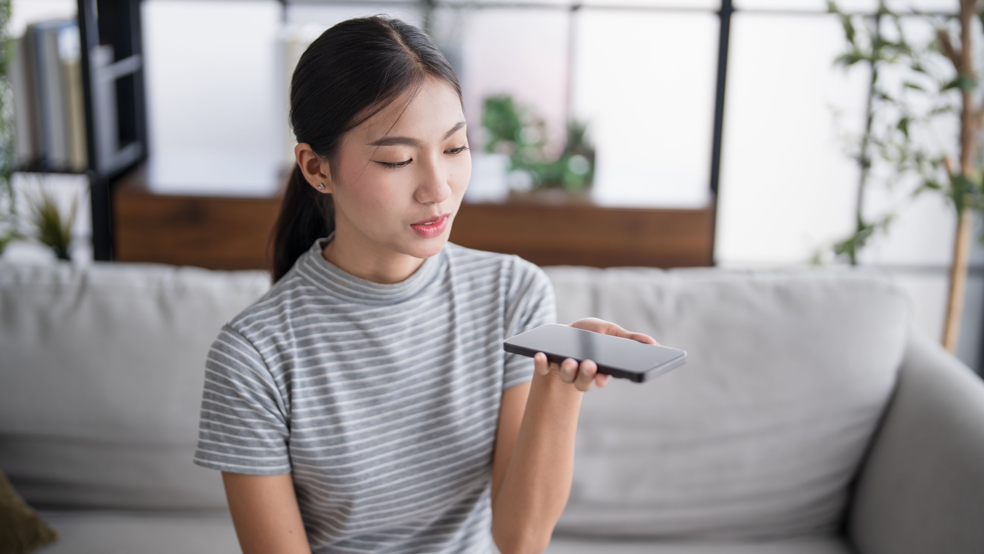 Asian woman using voice assistant on smartphone at home conversation with online assistantÂ Voice chat bot conversational AI Modern Technologies.